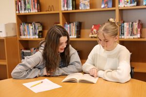 Image: Two students reading a book together in the library
