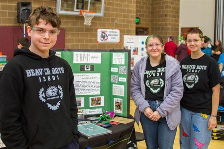 Grayson Tinker (9th), Alyssa VanCleef (11th), and Morrigan Chapman (10th) show the team's informational board used for outreach and recruting